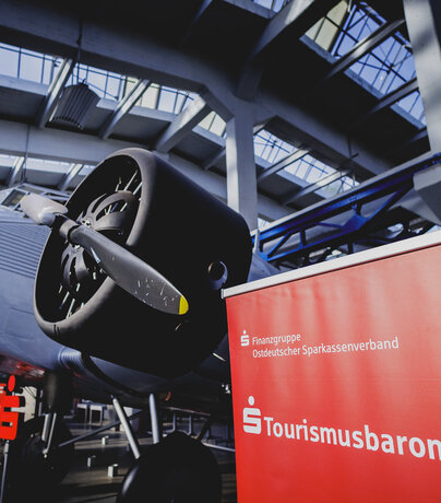 Sparkassen-Tourismusbarometer Sachsen-Anhalt Rotes Roll-up des Sparkassen-Tourismusbarometers vor einem historischen Junckers-Flugzeug in Dessau